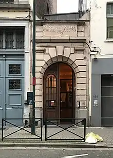 Photographie d'un bâtiment vu depuis la rue, avec un porche en pierre.