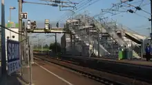 passerelle enjambant les voies avec les escaliers menant au quai central en cours de travaux et une volée d'escaliers provisoires soutenus par des échafaudages, au premier plan 2 voies et caténaires