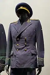 Un uniforme noir à boutons et galons dorés présenté sur un mannequin.