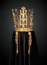 Couronne faite de bandeaux en or en forme d'arbres dressés aux feuilles d'or et pendentifs de jade (en forme de virgule). Photographie de face, sur fond sombre, la couronne étant posée sur un velours noir.
