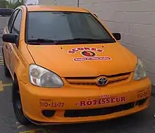 Voiture jaune avec écriture rouge sur le capôt stationné sur un terrain pavé avec un mur de béton à droite