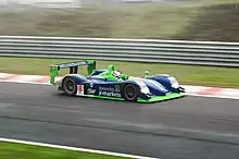 Photographie d'une voiture de sport-prototype bleue bleu, verte et blanche, vue de haut et de profil, sur une piste.