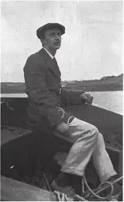  assis sur l'extrémité avant d'une barque, un homme coiffé d'un béret regarde au loin, cordes à la main.