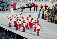 Un athlète en blanc et rouge tient le drapeau moldave puis un groupe d'athlètes biélorusses est derrière lui.