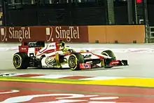 Monoplace blanche aux parties dorées et rouges, vue de trois-quarts, sous des projecteurs