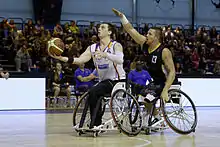 Joueur de basket fauteuil tirant au panier sous la pression d'un défenseur en contre-attaque.