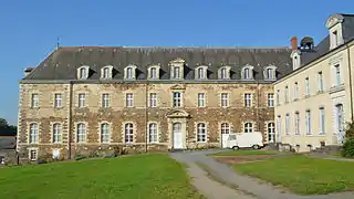 Bâtiment en pierre rousse, de trois étages, au toit d'ardoise.