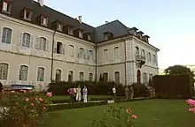 Photographie couleur d'un bâtiment de style classique, devant lequel des visiteurs se promènent dans un jardin.