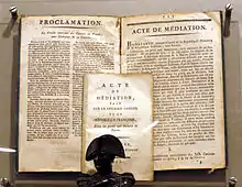 Un buste de Napoléon Bonaparte, avec derrière lui le texte de l'Acte de médiation.