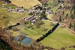 Photographie aérienne couleur d'un village devant lequel des ruines d'un édifice religieux sont visibles.