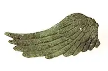 Photographie de l'aile droite d'une statuette de Victoire, de couleur verte. On distingue les plumes.