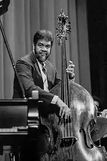 Un homme derrière un piano joue de la contrebasse.