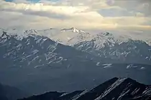 Des montagnes boisées en bas et enneigées plus haut, sous un ciel couvert.