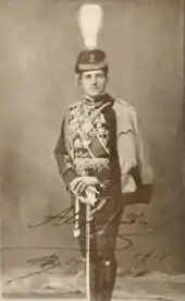photographie noir et blanc : portrait d'homme en pied, en grand uniforme, appuyé sur un sabre, avec un shako à plumet
