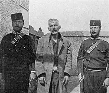 Photographie en noir et blanc montrant un homme à l'air hagard entouré de deux soldats.