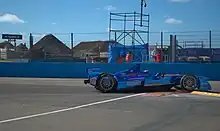 Photographie d'une monoplace de Formuel E bleu foncé, vue de profil, sur un vibreur, en ville.