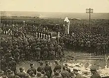 Photographie noir et blanc montrant une foule et l'aumônier au centre.