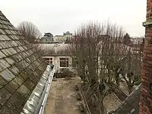 Photographie en couleurs d'une cour vue d'un toit la bordant, bordée d'une rangée d'arbres.