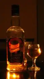 Dans la pénombre, une bouteille et un verre d’aquavit captent quelques rayons lumineux.