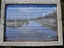 Vue d'une plaque explicative apposée à côté d'un vestige de monument antique.