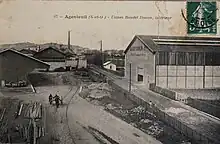Carte postale représentant une cours d'usine traversée par une voie ferrée.