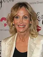 Photo en buste d'une femme avec des cheveux mi-longs et blonds, portant un manteau beige.