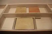 Vitrine présentant trois plaques de mortiers dont un de couleur jaune et l'autre de couleur rouge.