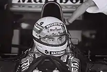 Photo en noir et blanc d'Ayrton Senna, casqué, au volant de sa monoplace, de face, en plan rapproché.