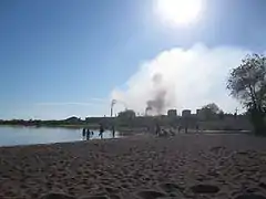 Une plage en avant plan et une usine au fond.