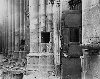 Deux piliers en pierre avec, à environ un mètre de hauteur, des trous de mine creusés. Au premier plan, une porte défoncée et un bénitier.