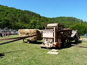 Batteuse Merlin (vers 1950). Vue sur l'ensachage des grains. La courroie sur le flanc de la machine entraîne une presse  séparée à  l'arrière.