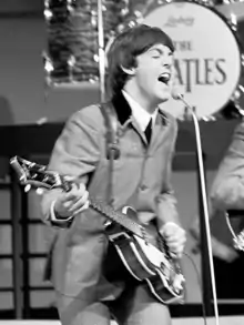 Paul McCartney en concert avec les Beatles, guitare basse en main, livrant une performance énergique