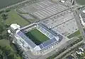 Photo aérienne du stade. On distingue la pelouse et les tribunes vides à l'intérieur, et les vastes parking à côté de l'édificice.