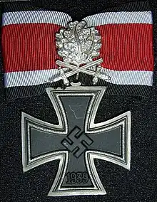 Distinction militaire métallique ayant la forme d'une croix pattée germanique avec un ruban rouge.