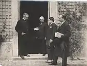 Groupe de personnages discutant sur le pas d'une porte.