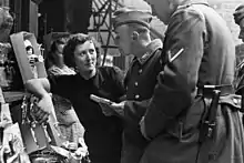 Photo noir et blanc montrant une commerçante et deux soldats allemands devant un étalage