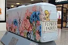 Photographie d'une maquette de bus entièrement floqué "Flower Fairies" avec le logotype utilisé par la franchise.