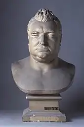 Photographie d'un buste, en marbre blanc, d'un homme corpulent, aux cheveux relevés.