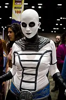 Femme portant un maquillage blanc intégral, à l’exception de rond noirs autour des yeux. Elle est vêtue de noir.