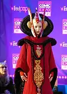 Femme portant une coiffe, un maquillage blanc et une robe rouge très élaborée.