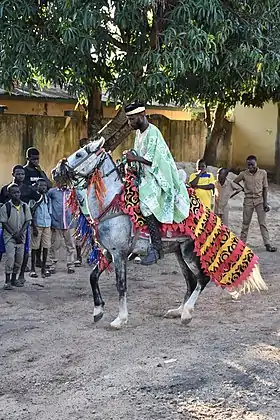 Homme noir en selle sur une cheval costumé, de nombreuses autres personnes le regardant.