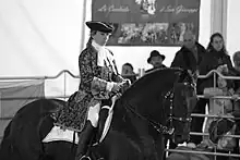 Photographie en noir et blanc représentant un Murgese de profil monté par une cavalière en costume baroque