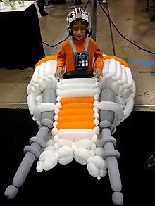 Enfant habillé en orange entouré de ballons blancs et orange.