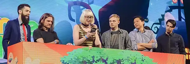 Six personnes derrière une tribune, une femme au centre lit sur son téléphone.