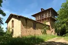photo couleur d'un bâtiment allongé ressemblant à une grange. Il est appuyé à une tour carrée ceinturée d'une galerie en bois.