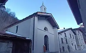 Photographie d'une chapelle entourée de maisons avec son clocher rénové et sa porte grillée.