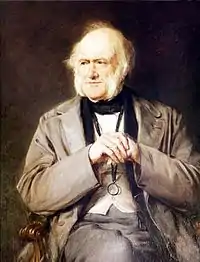 Portrait à l’huile. Lyell, au crâne fort dégarni mais portant de longs favoris blancs, est assis dans un fauteuil, les coudes posés sur les accoudoirs, mains croisées devant lui à hauteur de la poitrine. Il regarde légèrement sur sa droite.