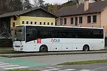 Photographie en couleurs d’un autocar blanc et noir stationné devant des bâtiment scolaires à Chavanod.