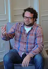 Homme brun barbu portant des lunettes avec un certain embonpoint.