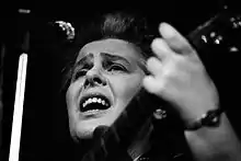 Photo en noir et blanc d'une femme qui chante en s'accompagnant à la guitare.